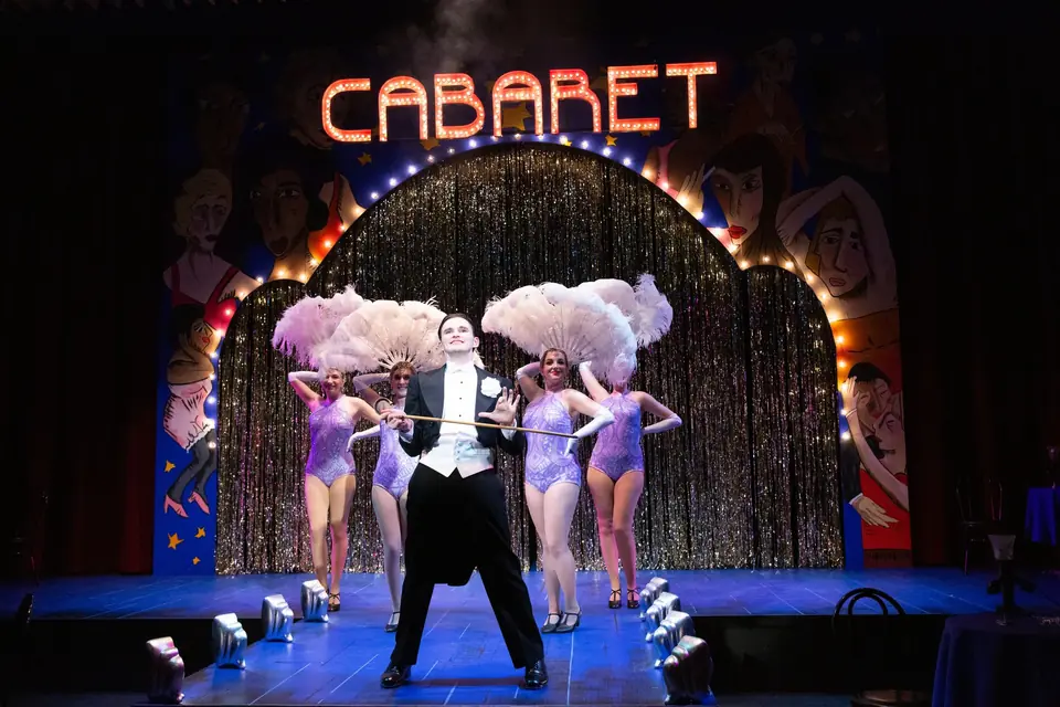The Kit Kat Klub: the Emcee and dancers under a marquee arch of bulbs spelling CABARET