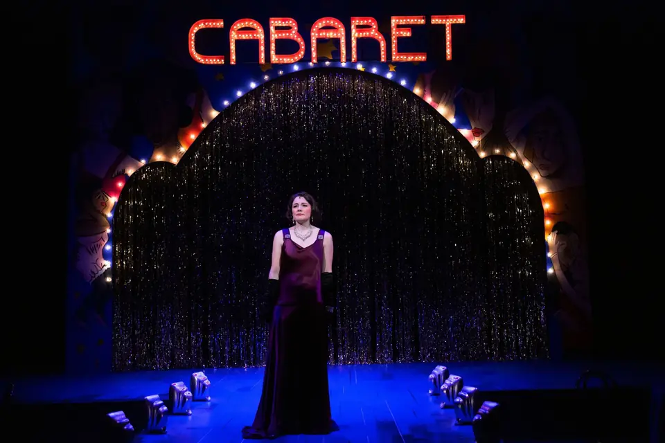 Sally Bowles alone at center stage beneath the lit CABARET arch