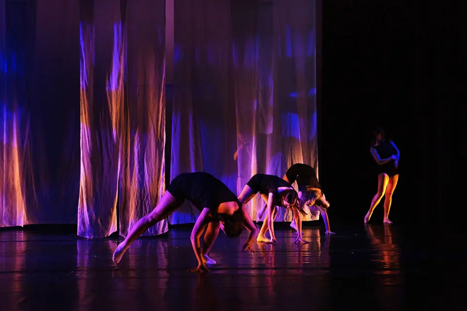 Dancers on a dark stage in front of a shimmering curtain lit in blue and magenta