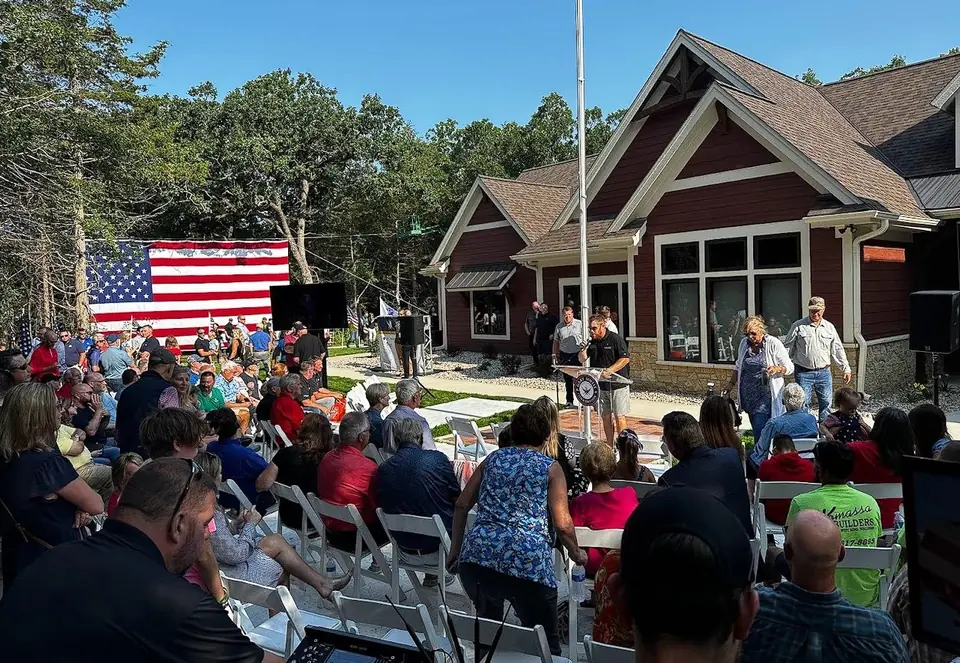 An outdoor ceremony with a large American flag and a crowd on the lawn